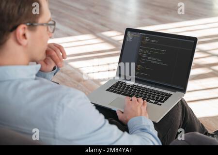 Close up shot of coder sitting with laptop on knees, working online on new IT product.  Stock Photo