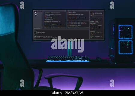 Empty programming workspace with big monitor screen shows code. Professional coder desk in neon lights. Data science concept Stock Photo