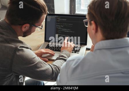 IT specialist giving personal programming lesson to man. Over shoulder view of coders colleagues working on new project together Stock Photo