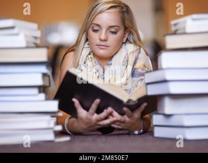 Knowledge resides between the covers. A beautiful young college student reading a textbook in the library. Stock Photo