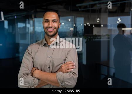 Portrait of hispanic successful businessman, successful man in shirt looking at camera with crossed arms, worker inside office near window. Stock Photo