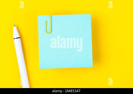 Blank blue notes paper and pen with a paper clip   on yellow background, for your text or message. Stock Photo