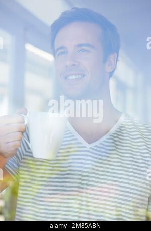 Peering through the glass. A young man standing and looking out of a window. Stock Photo
