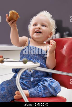 I can feed myself. a cute young baby sitting in a high chair eating. Stock Photo