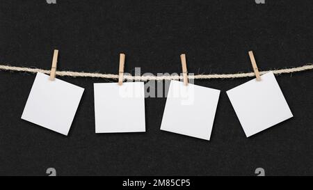 Four blank post it reminders and clothespins attached to a rope on retro black paper background. Stock Photo