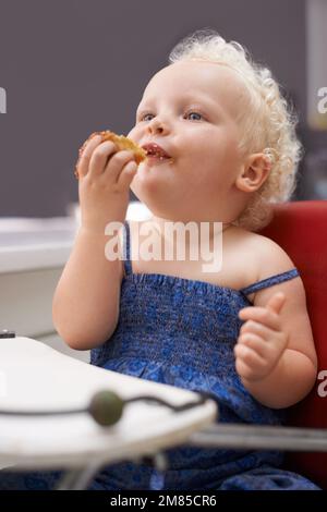 BAby is hungry. a cute young baby sitting in a high chair eating. Stock Photo