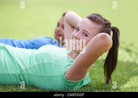 Toning our tummies. young women doing sit ups on the grass outside. Stock Photo