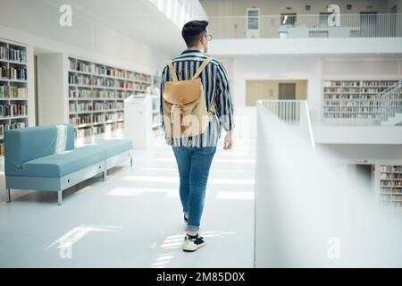 Backpack, library and education with a man student walking in a university bookstore for learning or development. Back, college and research with a Stock Photo