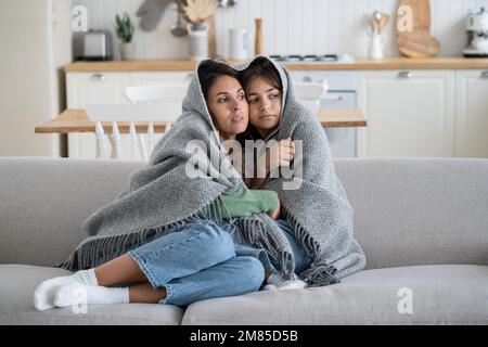 Unhappy European family, mother and daughter covered with blanket freezing in cold apartment Stock Photo