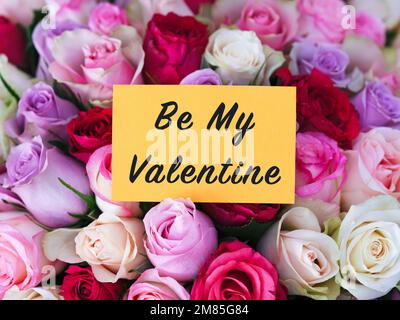 A yellow greeting card with words Be My Valentine laying on a big bouquet of colorful roses Stock Photo