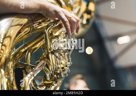 A man's hand is seen playing a large brass instrument tuba as part of an orchestra during a ceremony. Face not shown. Concept of music, performance, or celebration. Stock Photo