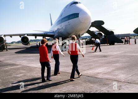 Red Coat volunteers walk out to greet military personnel and their families arriving on a commercial Boeing 747 aircraft. The Red Coats are passenger service volunteers from the Yokota Officers' Wives Club. They assist regular terminal workers by greeting new arrivals and guiding them through terminal processing and customs procedures. Base: Yokota Air Base Country: Japan (JPN) Stock Photo