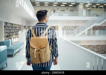 Backpack, library and study with a man student walking in a university bookstore for education or learning. Back, college and research with a male Stock Photo