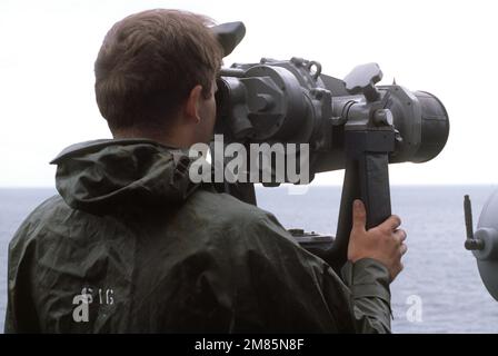A crewman aboard the guided missile cruiser USS YORKTOWN (CG-48) looks through a pair of high-powered binoculars while standing watch. Country: Unknown Stock Photo