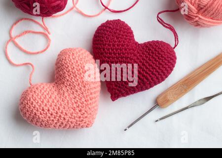Two crocheted amigurumi pink hearts with a crochet hooks on a white background. Valentine's banner top view horizontal Stock Photo