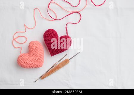 Two crocheted amigurumi pink hearts with a crochet hooks on a white background. Valentine's banner top view with copyspace Stock Photo