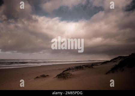 A dramatic sky with stormy clouds over the dunes and the Atlantic Ocean in a wild and empty beach. Moody tones and desaturated colors. Quiaios Beach Stock Photo