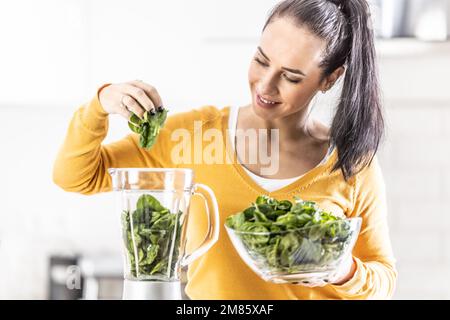 Smiling woman making spinach smoothie, putting leaves in blender. Stock Photo