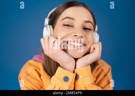 Portrait of cheerful teenager in headphones looking at camera isolated on blue Stock Photo