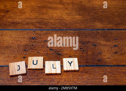 July word on letter tiles on wooden background with copy space Stock Photo