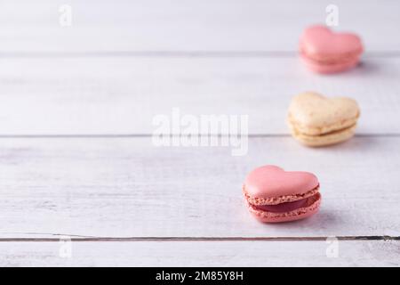 Three heart shaped, cream filled French Macaroons on white wooden Background. Traditional confectionery for Valentine's Day, Mother's Day or Wedding. Stock Photo