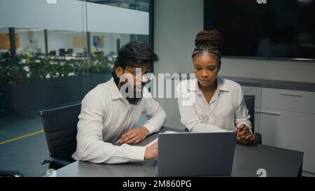 Business partners multiracial diverse company coworkers colleagues in office Indian man and African woman solving online problem with laptop computer Stock Photo