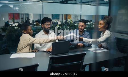 View from behind glass African American female team leader company CEO check strategy with diverse colleagues paperwork documents multiracial business Stock Photo
