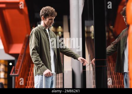 smiling and curly man pressing call button of elevator in modern hotel,stock image Stock Photo
