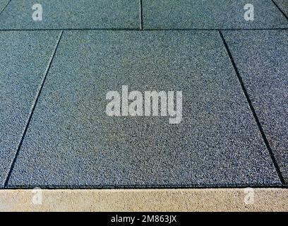 Padded granular square rubber tile sports ad safety flooring in outdoor playground. textured gray concrete edge trim. playground and exercise, workout Stock Photo