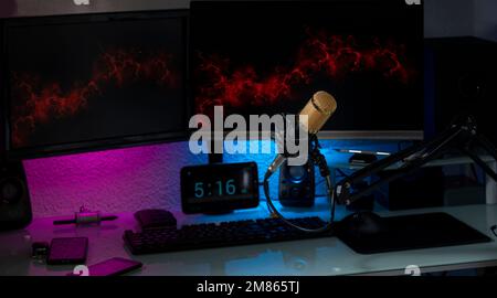 Condenser microphone in gamer setup with monitors, keyboard, mouse and colored lights. Stock Photo