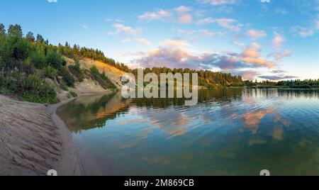 A high cliff on the shore of a lake with colorful clouds in the sky at sunset Stock Photo