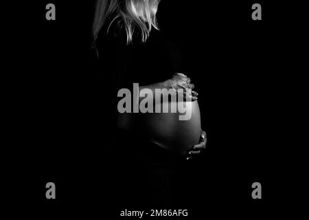 Black and white view of pregnant woman gently holds her belly and caring about her health. Pregnancy, maternity, preparation and expectation concept. Stock Photo