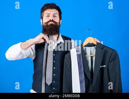 How about this tie. Brutal hipster holding colorful tie collection and suit jacket. Bearded man matching neck tie color to formal coat. Choosing a Stock Photo