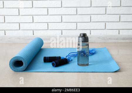 Sports water bottle with skipping rope on mat near white brick wall Stock Photo