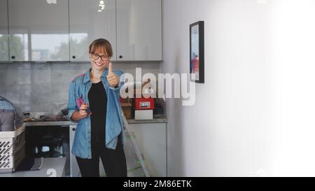 medium full shot of a young woman holding a screwdriver and showing thumb up in the kitchen, repair concept. High quality photo Stock Photo
