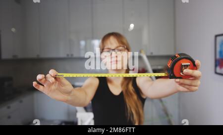 medium shot of a long-haired woman with glasses holding an open measuring tape, tools for renovation in the background. High quality photo Stock Photo