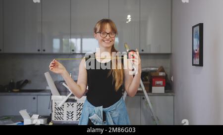 happy and satisfied woman holding an open measuring tape in the kitchen, tools behind her. High quality photo Stock Photo