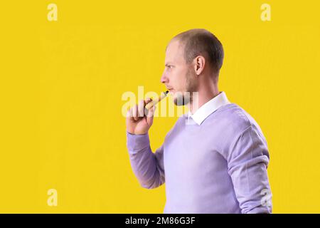 Young man smoking disposable electronic cigarette on yellow background Stock Photo