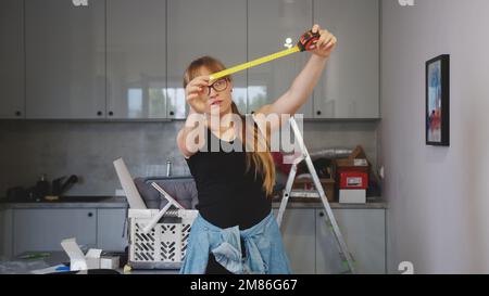 medium shot of a young woman holding an open measuring tape upwards and measuring something in the kitchen, repair concept. High quality photo Stock Photo