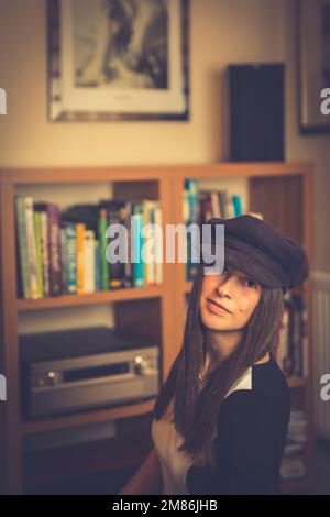 British female, with long hair & wearing 1970s style hat, posing for photograph isolated indoors at home in a typical UK lounge/living room. Stock Photo