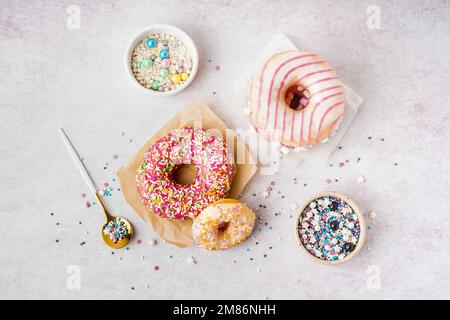 Parchments with different delicious donuts and bowls of sprinkles on white table Stock Photo