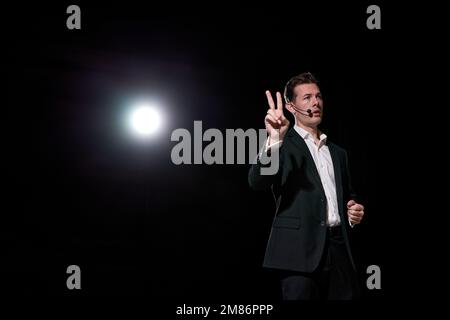 Man speaking through microphone in dark conference hall, on stage, performance. Person in suit says about marketing and management for successful sale Stock Photo