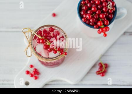 Summer drink with white sparkling wine. Homemade refreshing fruit cocktail or punch with champagne, red currant and ice cubes on a white wooden Stock Photo