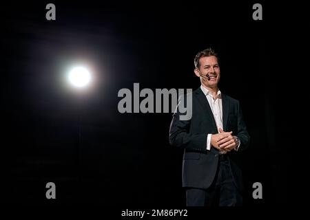 Man speaking through microphone in dark conference hall, on stage, performance. Person in suit says about marketing and management for successful sale Stock Photo