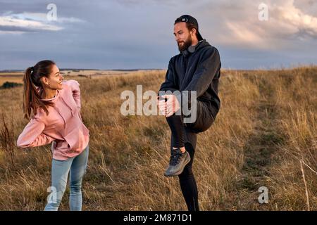 Skillful couple warming up before running, stertching legs with concentration, warm up muscles. Man and woman in sportive clothes motivated, standing Stock Photo