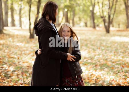 Delightful carefree family of young mother and blond daughter in leather jacket embracing, look camera in autumn forest Stock Photo