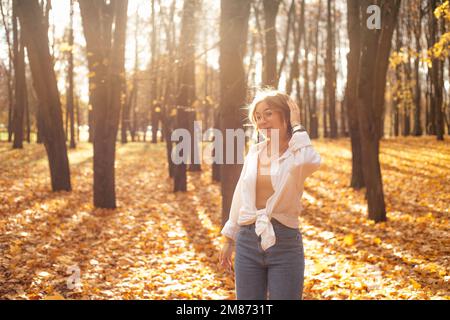 Cheerful, fairy, stylish smiling blond woman in eyeglasses walk in golden forest, straighten hair and joying warm autumn Stock Photo