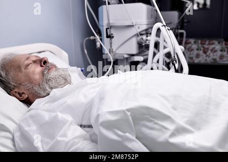 covid-19 patient with Endotracheal Tube In Mouth Lying On Medical Couch, Bed in hospital. senior sick person alone in ward room, suffering from diseas Stock Photo