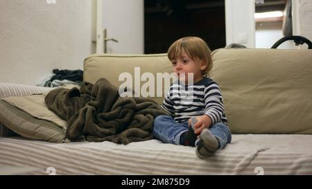 Baby blond toddler sitting on sofa watching cartoon hypnotized by media Stock Photo