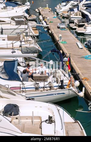 At the Club Nautico of Porto Cristo, Mallorca three friends enjoy the sunny day on a sailboat. Stock Photo